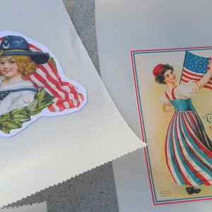 May include: Two white paper bags with patriotic images. One shows a child in a sailor suit with an American flag and a laurel wreath. The other has a woman holding a flag with the text "Three cheers for the Red, White and Blue."