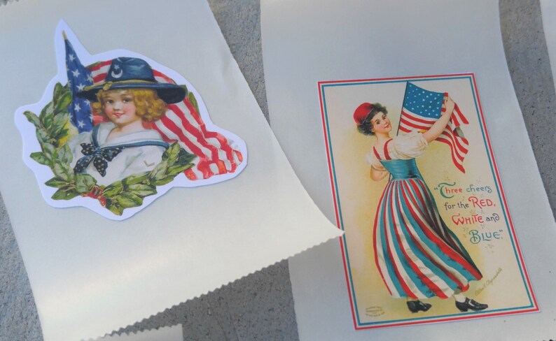 May include: Two white paper bags with patriotic images. One shows a child in a sailor suit with an American flag and a laurel wreath. The other has a woman holding a flag with the text "Three cheers for the Red, White and Blue."