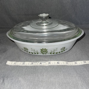 May include: White oval casserole dish with a clear glass lid and a clear glass knob. The dish has a green floral pattern around the rim. A measuring tape is next to the dish.