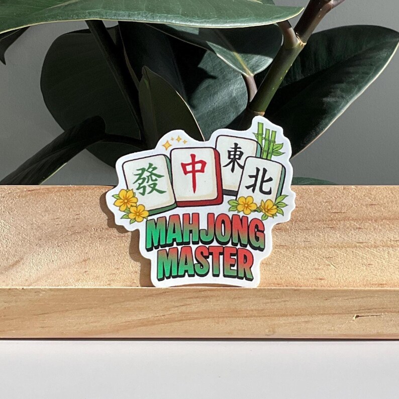 May include: A sticker featuring a Mahjong Master design. The sticker has four Mahjong tiles with Chinese characters and the words "Mahjong Master" in green. Yellow flowers and bamboo stalks decorate the edges.
