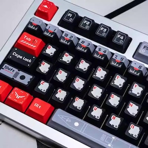 Puede incluir: Primer plano de un teclado mecánico con marco plateado y teclas negras. Las teclas de acento rojo incluyen Tab, Caps Lock y Alt. Las teclas presentan letras y símbolos blancos, con un diseño futurista. El teclado mide unos 30 cm de ancho.