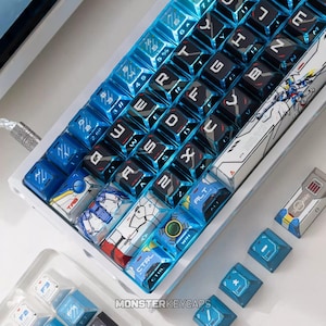 Puede incluir: Un teclado mecánico con teclas brillantes en azul y blanco con impresiones gráficas personalizadas, incluyendo ilustraciones de estilo robótico y letras blancas. El teclado tiene un marco blanco y un cable trenzado, con teclas sueltas.