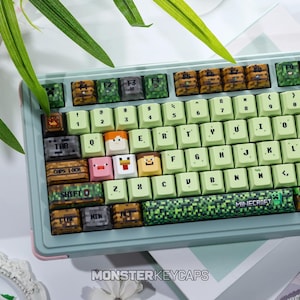 May include: A mechanical keyboard featuring custom keycaps with Minecraft-themed designs, including pixelated textures, character faces, and the Minecraft logo on the spacebar. The keyboard has a light green frame and light green alphanumeric keys.