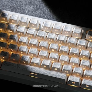 May include: A mechanical keyboard featuring white keycaps with a grey feather pattern and backlit orange lettering. The keys display standard QWERTY layout characters, function keys, and the text MONSTERKEYCAPS printed on the spacebar.