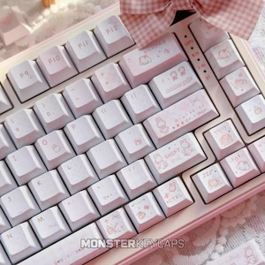 Könnte beinhalten: Eine mechanische Tastatur in Hellrosa und Weiß mit individuell gestalteten Tastenkappen, die mit kleinen Illustrationen von Hasen, Schleifen und Sternen verziert sind. Die Tasten tragen Beschriftungen wie BACKSPACE, SHIFT, CTRL und ALT.