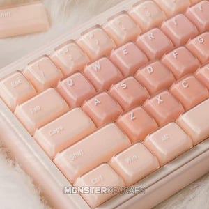Op de afbeelding: Een mechanisch toetsenbord met doorschijnende, glanzende, licht perzikkleurige toetsen met witte letters. De toetsen hebben een afgerond, geleiachtig uiterlijk. De tekst MONSTERKEYCAPS is zichtbaar in het midden onderaan het toetsenbordframe.