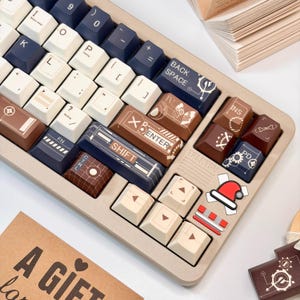 May include: A beige mechanical keyboard with custom keycaps in navy blue, brown, and cream colors. The keycaps feature various icons and text, including "SHIFT" and "ENTER". A Santa hat sticker is visible.