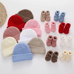 Könnte beinhalten: Eine Sammlung gestrickter Baby-Mützen und -Schuhe in verschiedenen Farben. Die Mützen sind in Rot-, Braun-, Rosa-, Weiß-, Beige- und Blautönen gehalten. Die Schuhe sind in passenden Farben, darunter Beige, Blau, Rosa, Rot, Braun und Weiß.