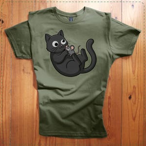 May include: Olive green t-shirt featuring a cartoon black cat holding a gray mouse. The cat has large, round eyes and a playful expression. The design is centered on the shirt, which has a crew neck and short sleeves. The shirt is made of a soft material.