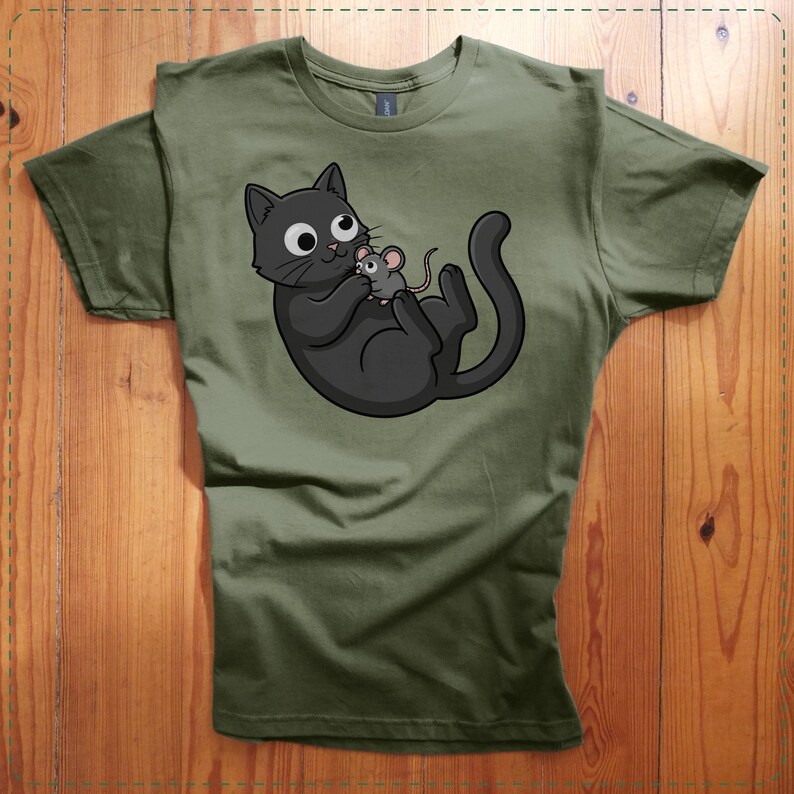 May include: Olive green t-shirt featuring a cartoon black cat holding a gray mouse. The cat has large, round eyes and a playful expression. The design is centered on the shirt, which has a crew neck and short sleeves. The shirt is made of a soft material.