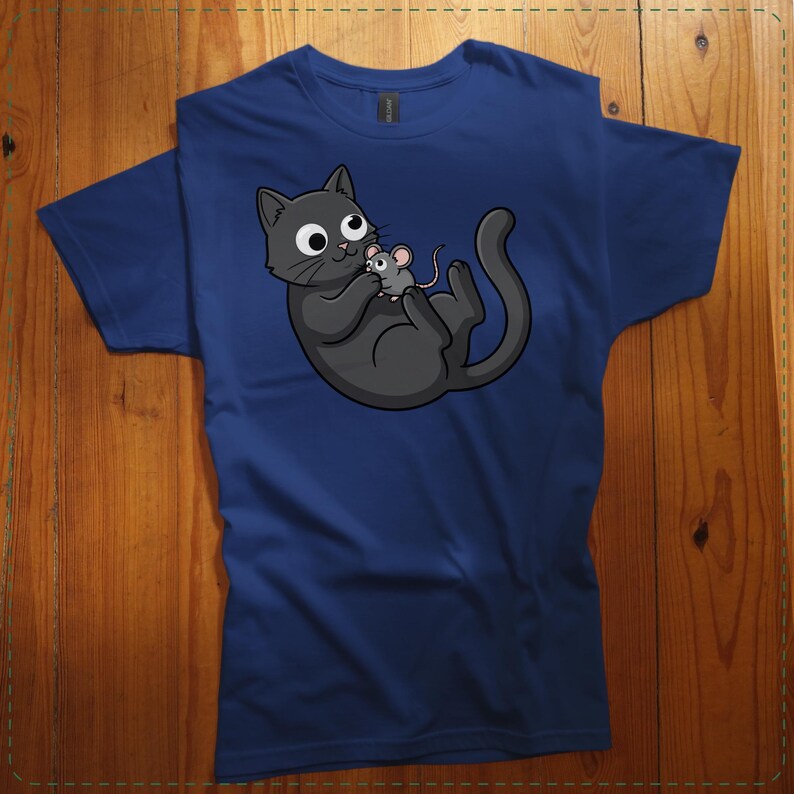 May include: Navy blue t-shirt featuring a cartoon illustration of a gray cat holding a gray mouse. The cat has large, round eyes and a playful expression. The design is centered on the shirt.
