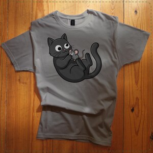 May include: A gray t-shirt featuring a cartoon cat holding a mouse. The cat is black with large white eyes and a pink nose. The mouse is gray. The design is centered on the shirt.