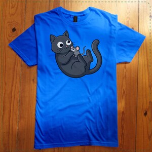 May include: Bright blue t-shirt featuring a cartoon illustration of a gray cat holding a gray mouse. The cat has large, round eyes and a playful expression. The shirt is made of a soft material and has short sleeves.