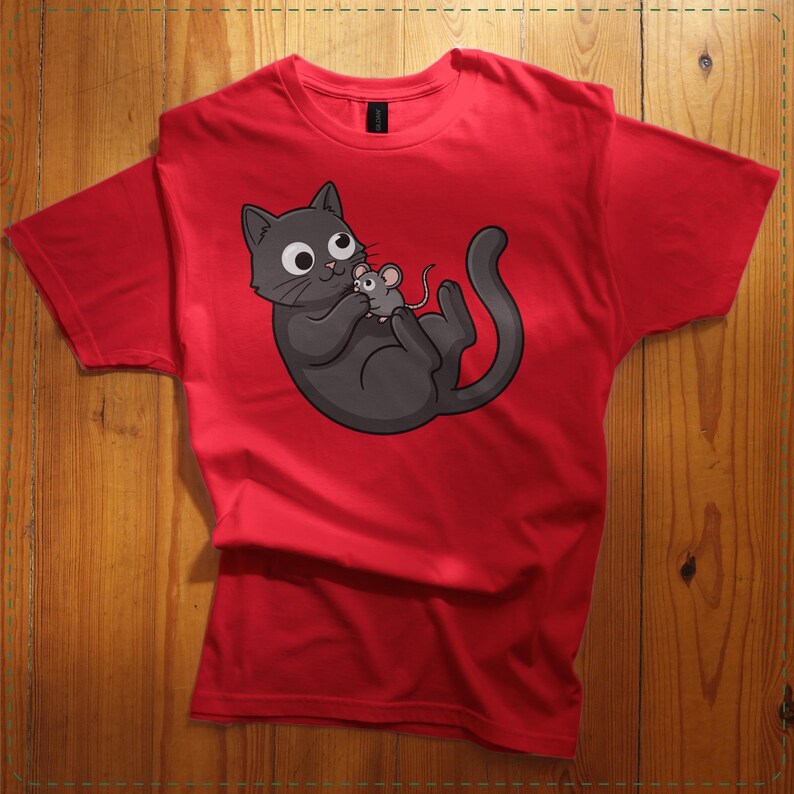 May include: Red t-shirt featuring a cartoon cat and mouse graphic. The black cat is lying on its back, holding a gray mouse. The cat has large, round eyes and a playful expression. The t-shirt is made of a soft material.