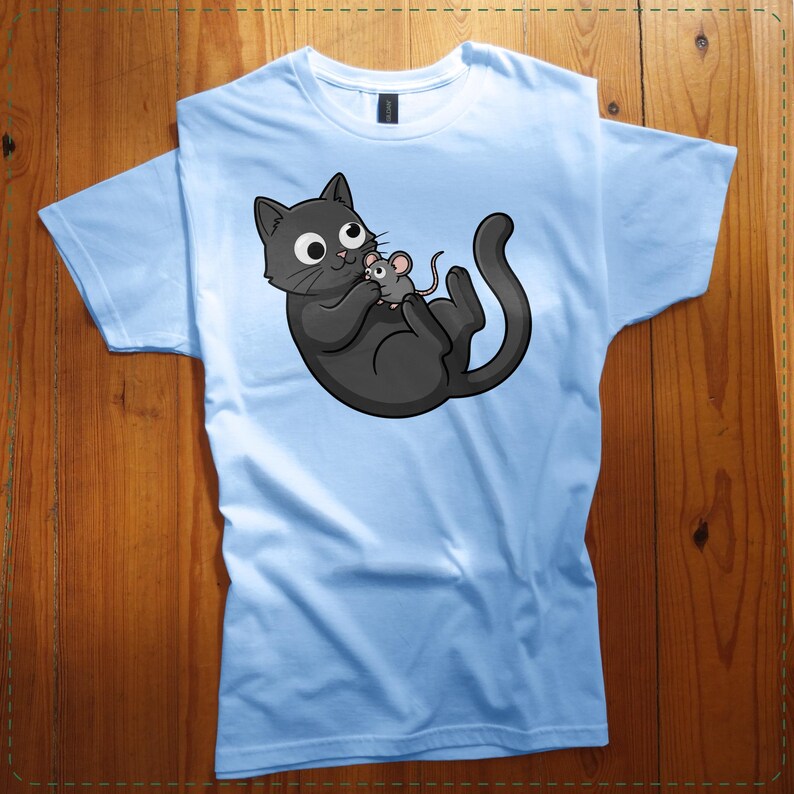 May include: Light blue t-shirt featuring a cartoon illustration of a black cat holding a gray mouse. The cat has large, round eyes and a playful expression. The shirt is made of a soft material and is suitable for casual wear.