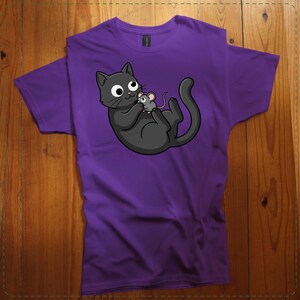 May include: Purple t-shirt featuring a cartoon cat and mouse graphic. The black cat is lying on its back, holding a small gray mouse. The design is centered on the shirt, with the cat and mouse in a playful pose. The shirt is made of a soft material.