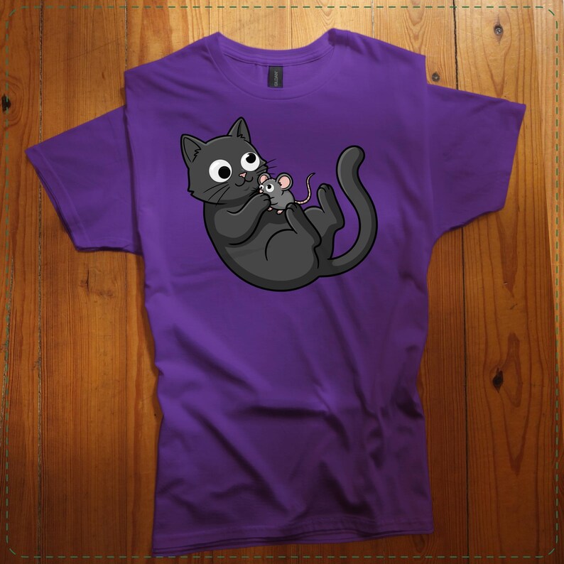 May include: Purple t-shirt featuring a cartoon cat and mouse graphic. The black cat is lying on its back, holding a small gray mouse. The design is centered on the shirt, with the cat and mouse in a playful pose. The shirt is made of a soft material.