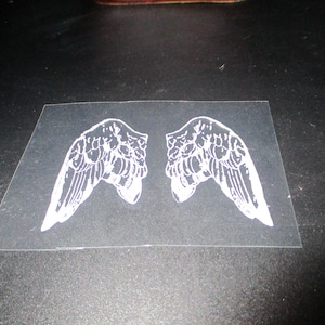 May include: Two white angel wings printed on a clear sheet of paper.