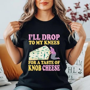 May include: Black t-shirt with the text "I'LL DROP TO MY KNEES FOR A TASTE OF KNOB CHEESE" in pink and yellow. The graphic features a person kneeling before a large wedge of cheese.