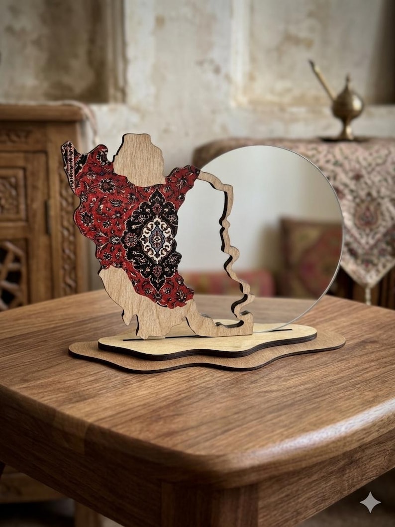 May include: A decorative tabletop mirror featuring a wooden frame shaped like the map of Iran. The left side of the wooden frame is decorated with a detailed red, black, and white floral pattern, while the right side holds a circular mirror.