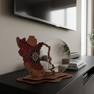 May include: A decorative wooden sculpture featuring a cutout of the state of Wisconsin, with a red and black patterned inlay on the left side and a circular mirror attached to the right, all mounted on a layered, irregular wooden base.