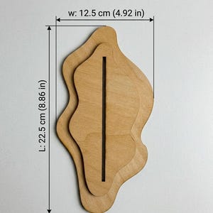 May include: A light brown wooden display stand with an organic, wavy shape and a central vertical slot. The stand measures 4.92 inches in width and 8.86 inches in length, as indicated by the text and dimension lines visible on the image.