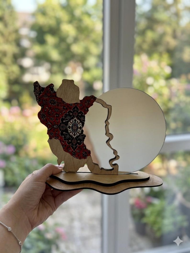 May include: A decorative wooden stand featuring a cutout map of Iran on the left side, decorated with a red, black, and white intricate floral pattern. A circular mirror is attached to the right side, all mounted on a layered, wavy wooden base.