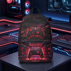 Puede incluir: Mochila negra con un diseño de mando de videojuego rojo y negro. La palabra "GAMER" está impresa en la parte delantera, con "LEVEL UP" debajo. La mochila tiene un asa superior y dos correas para los hombros.
