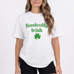 Könnte beinhalten: Weißes T-Shirt mit dem Text "Basically Irish" in Grün und einer grünen Kleeblatt-Grafik. Das Shirt hat kurze Ärmel und einen Rundhalsausschnitt. Das Model trägt schwarze Shorts.