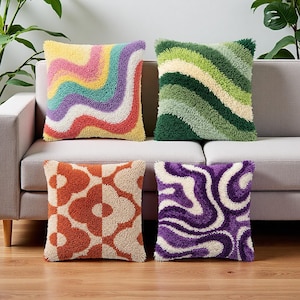 Peut inclure: Quatre coussins carrés à la surface touffetée texturée. L'un présente des rayures ondulées multicolores, un autre des rayures ondulées vertes, un troisième un motif floral orange et crème, et le dernier des lignes ondulées abstraites violettes.