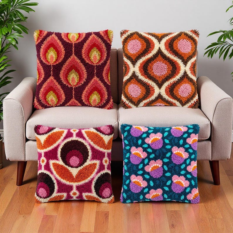 May include: Four square throw pillows with textured punch needle embroidery. The top left features red and yellow flame shapes on a dark purple background. The top right has orange and pink geometric patterns. The bottom left shows pink and orange floral motifs on a magenta base. The bottom right displays pink and purple flowers on a dark teal background.