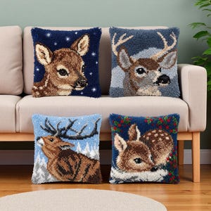 以下が含まれることがあります： 鹿のテクスチャード加工されたパンチニードルデザインが施された4つの正方形のクッション。左上は星空のダークブルーの背景に子鹿、右上は雪景色の中に雄鹿、左下は雄鹿、右下は子鹿が描かれています。