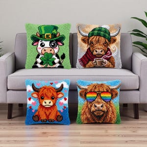 Könnte beinhalten: Vier dekorative Kissen mit skurrilen Highland-Kuh-Designs. Eine Kuh trägt einen grünen Hut und hält ein Kleeblatt, eine andere trägt einen Schal und hält eine Tasse, eine dritte hat Herzen und die letzte trägt eine Regenbogen-Sonnenbrille. Die Kissen liegen auf einem grauen Sofa.
