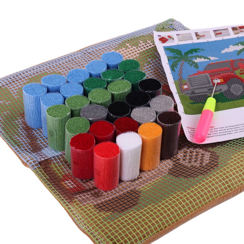 May include: A latch hook kit featuring a grid-patterned canvas with a printed design of a red vehicle and palm trees, a set of pre-cut yarn bundles in various colors including blue, green, red, white, and black, and a latch hook tool with a pink handle.