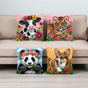 Pode incluir: Quatro almofadas decorativas com desenhos de animais. As almofadas apresentam uma vaca, um filhote de tigre, um panda e um corgi, cada um rodeado por detalhes florais. As almofadas têm uma aparência texturizada e bordada, sobre um fundo neutro.