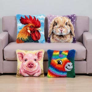 Puede incluir: Cuatro cojines decorativos con diseños de animales. Los cojines presentan un gallo, un conejo, un cerdo y un burro colorido. Cada cojín tiene una apariencia texturizada y afelpada y está colocado sobre un sofá rosa claro.