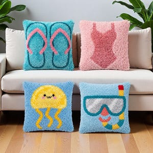 Peut inclure: Quatre coussins carrés à la surface en bouclette texturée. L'un est turquoise avec des tongs roses, un rose clair avec un maillot de bain une pièce, un bleu clair avec une méduse jaune et un bleu clair avec un masque de plongée et un tuba.