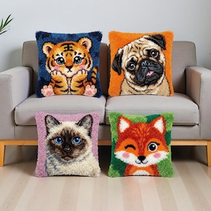 May include: Four decorative throw pillows with animal designs. The pillows feature a tiger, pug, Siamese cat, and fox. Each pillow has a square shape and a textured, tufted appearance. The pillows are placed on a gray sofa.