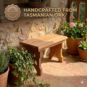 May include: A rectangular wooden bench with a light brown finish and a smooth top surface. The bench features four sturdy legs with a cutout design. The text "HANDCRAFTED FROM TASMANIAN OAK" is displayed above the bench in gold lettering.