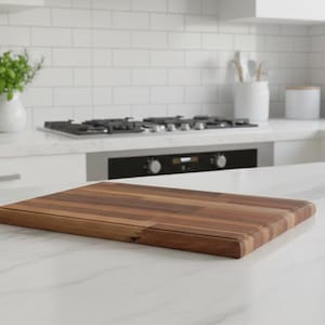 May include: A rectangular wooden chopping board with a dark brown finish sits on a white countertop. The kitchen setting includes a stainless steel knife block, a gas hob, and a white vase with greenery.