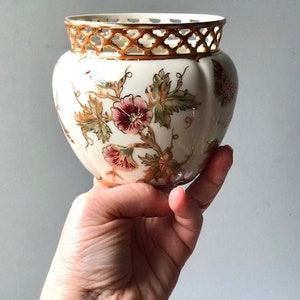 May include: A white ceramic planter with a gold rim and floral design. The planter has a lattice-like design around the top rim.