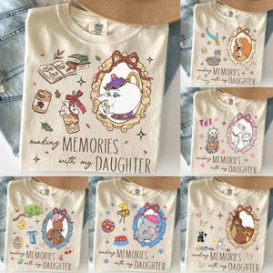 May include: Cream-colored t-shirts with various cartoon character designs inside ornate frames. Each shirt has the phrase "making memories with my daughter" printed below the design. The designs include a teapot, dogs, cats, and other characters.