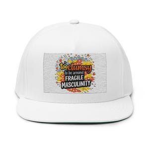 Peut inclure: Casquette de baseball blanche à visière plate. L'avant de la casquette présente un écusson rectangulaire avec le texte "too clumsy to be around FRAGILE MASCULINITY" dans une police colorée et ludique. Le patch a un fond texturé avec des accents orange, jaune et rouge.