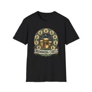 Op de afbeelding: Zwart t-shirt met een cirkelvormig ontwerp met de tekst "Drumming Circle". Het ontwerp bevat illustraties van drums, een halve maan en dierenriemfiguren in teal en goud. Het t-shirt is gemaakt van zacht materiaal.