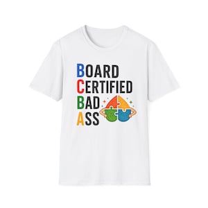 May include: White t-shirt featuring the text "BOARD CERTIFIED BAD ASS" in blue, red, green, and orange. The design includes a puzzle piece graphic with arms and a starburst.