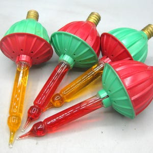 May include: Four vintage bubble light bulbs featuring a brass screw base, a ribbed plastic cap in alternating red and green colors, and a glass tube filled with liquid that glows in either a vibrant yellow or a deep red color when illuminated.