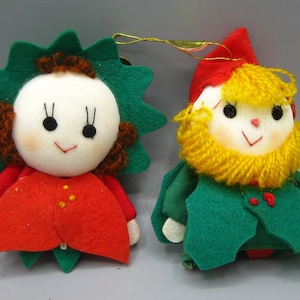 May include: Two vintage Christmas ornaments. One is a doll with a white face, green spiky hair, and a red outfit. The other is a gnome with a red hat, yellow beard, and green outfit. Both have smiling faces.