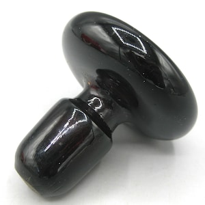 May include: A glossy black bottle stopper with a rounded top and a cylindrical base. The stopper is designed to fit into the neck of a bottle. The smooth, reflective surface suggests a polished finish.