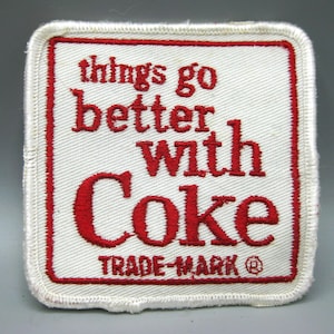 May include: A square embroidered patch with a white background and a red border. The text "things go better with Coke" is stitched in red thread in the center, with "TRADE-MARK" and a registered trademark symbol printed in red below the text.