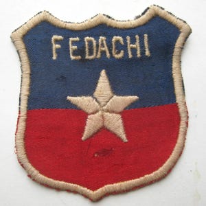 May include: A shield-shaped patch with a blue upper half and a red lower half. The word "FEDACHI" is embroidered in tan thread across the top. A tan star is centered on the patch. The patch has a tan border.